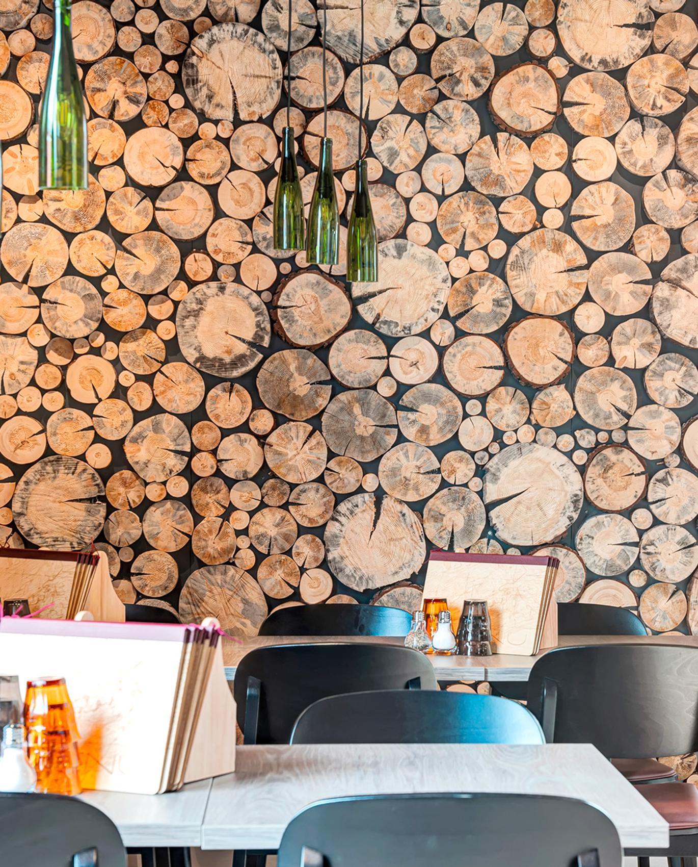 Ravintolan tunnelmallinen sisustus, jossa puukerrosseinämä, kauniisti valaistut valaisimet ja tyylikkäät pöydät. Sisustus tuo esiin luonnonläheisyyttä ja modernia muotoilua. Kuva: PKO.