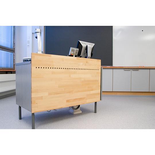 Opetuskäyttöön suunniteltu puinen opettajanpöytä Länsikadun koulun luokkahuoneessa. Pöydässä yhdistyvät käytännöllisyys ja esteettisyys, sisältäen modernin teknologian sijoitusratkaisut.