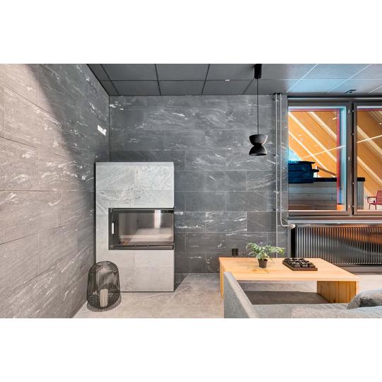 Moderni sisätila, jossa harmaasta kivestä valmistettu takka, minimalistinen musta valaisin ja vaaleasta puusta tehty matala pöytä. Suuret ikkunat tarjoavat näkymän ulkoterassille, jossa näkyy katettu alue. Kuva: PKO.