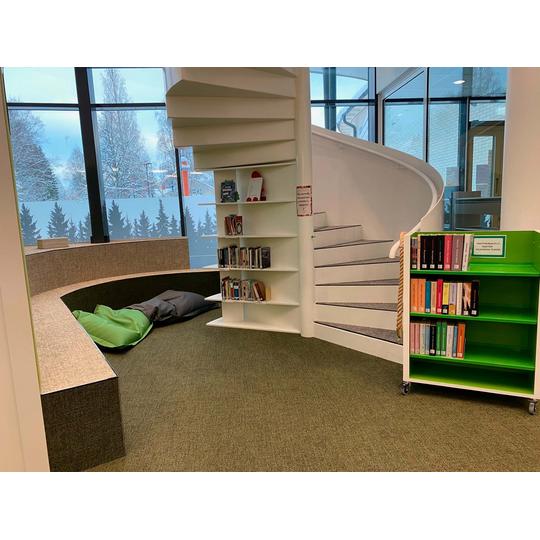 Karsikon kirjaston lukutila, jossa on py&ouml;re&auml; istuma-alue, sisustetyynyj&auml; ja moderni valkoinen kierreportaikko, joka yhdist&auml;&auml; eri kerrokset harmonisesti.