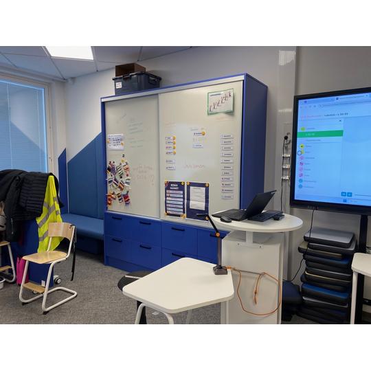 Nykyaikainen luokkahuone, jossa on suuri taulu, liikuteltavat pöydät sekä runsaasti säilytystilaa.