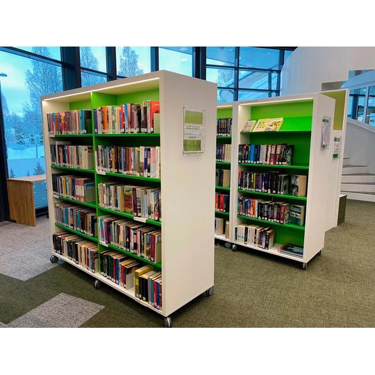 Karsikon kirjaston modernit ja siirrettävät kirjahyllyt, joissa yhdistyvät valkoinen runko ja vihreät hyllylevyt, osana Joen Erikoiskalusteen toteuttamaa tilaratkaisua.