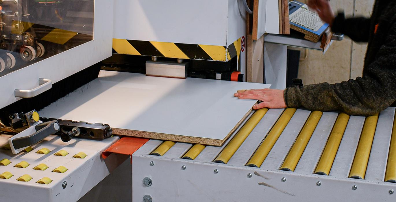 Puunty&ouml;st&ouml;kone k&auml;yt&ouml;ss&auml; Joen Erikoiskalusteen tuotantotiloissa, ty&ouml;ntekij&auml; k&auml;sittelee laminaattilevy&auml; koneella.