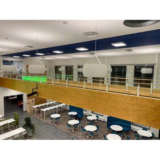 Lehmon koulun avara ruokasali Kontiolahdella, jossa modernit pyöreät ja suorakulmaiset pöydät sekä värikkäät tuolit luovat kutsuvan ilmapiirin. Kattovalaisimet ja puupintainen kaide erottuvat tyylikkäässä sisustuksessa.