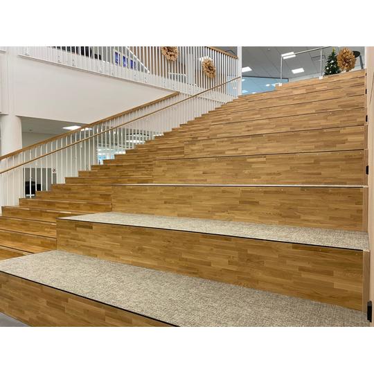 Moderni puinen portaikko, joka tarjoaa sek&auml; istumapaikkoja ett&auml; kulkuyhteyden eri kerroksiin.