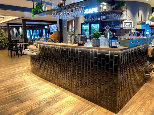 Moderni ja tyylikäs baaritiski, jossa yhdistyvät tumma laattapinta, puupinta ja metalliset yksityiskohdat. Baaritiski on varustettu valaistuksella ja riittävällä työtilalla.