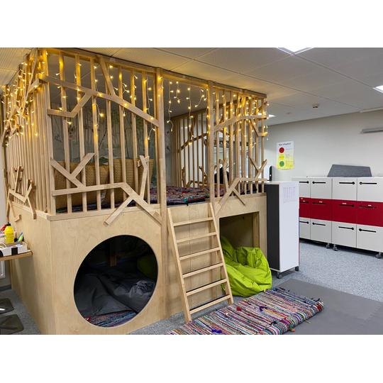 L&auml;nsikadun koulun viihtyis&auml; oleskelutila, jossa on puinen leikkim&ouml;kki, oksakuvioita, koristelamppuja ja pehmeit&auml; istuintyynyj&auml;.