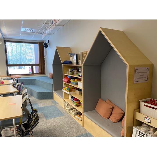 Länsikadun koulun luokkahuone, jossa on oppilaspöytiä, puusäilytyskalusteita, talonmuotoisia lukunurkkauksia pehmustetyynyillä sekä portaikko oleskelualueeksi.