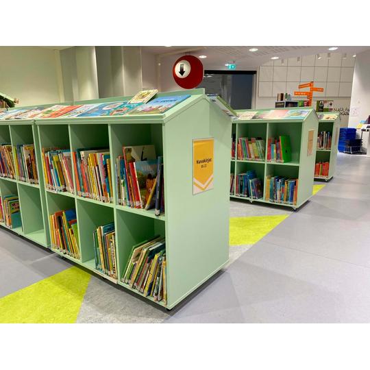 Joensuun p&auml;&auml;kirjaston lastenosaston matalat, vaaleanvihre&auml;t hyllyt, joissa on v&auml;rikk&auml;it&auml; lastenkirjoja. Jokaisella hyllyll&auml; on selke&auml; nimikyltti, kuten 'Kuvakirjat,' ja hyllyjen p&auml;&auml;ll&auml; on esill&auml; suurikokoisia kuvakirjoja.