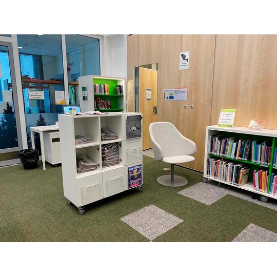 Karsikon kirjaston lukunurkkaus, jossa on moderni valkoinen nojatuoli, py&ouml;rill&auml; liikkuva s&auml;ilytyshylly sanomalehdille ja kirjoille sek&auml; valikoima aikakauslehti&auml;.