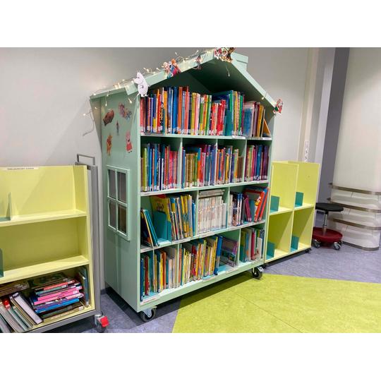 Joensuun p&auml;&auml;kirjaston lastenosaston hylly, joka on talon muotoinen ja t&auml;ynn&auml; v&auml;rikk&auml;it&auml; lastenkirjoja. Hyllyn yl&auml;osaa koristavat valonauhat ja hahmofiguurit, kuten Muumipeikko ja Peppi Pitk&auml;tossu. Vieress&auml; on vaaleankeltaisia lis&auml;hyllyj&auml; kirjoille.