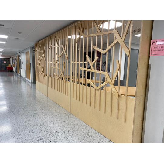Länsikadun koulun käytävällä sijaitseva puinen tilanjakaja, jossa on oksakuvioita ja avattuja säleitä.