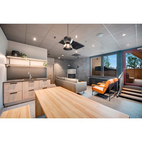 Tyylik&auml;s oleskelutila, jossa moderni keitti&ouml;, vaaleasta puusta valmistettu ruokap&ouml;yt&auml;, harmaa sohva, oranssit nojatuolit ja takka. Suuret ikkunat ja ulosk&auml;ynti johtavat terassille, jossa on palju ja n&auml;kym&auml;t ulos. Kuva: PKO.