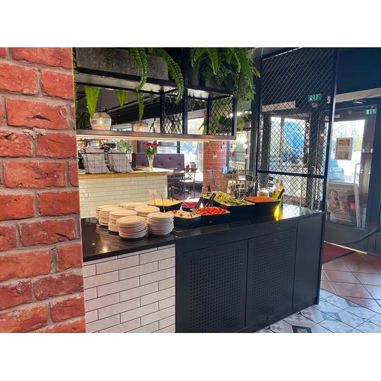 Rosso Joensuun salaattip&ouml;yt&auml;, jossa musta taso, valkoinen laattapinta ja tiilisein&auml; yhdistyv&auml;t vehreisiin viherkasveihin ja moderniin ravintolasisustukseen.