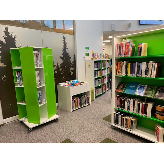 Karsikon kirjaston kirjahyllyt ja pyörillä liikkuva vihreä esittelyteline, jotka tarjoavat modernin ja käytännöllisen säilytysratkaisun erilaisille kirjoille ja lehdille.
